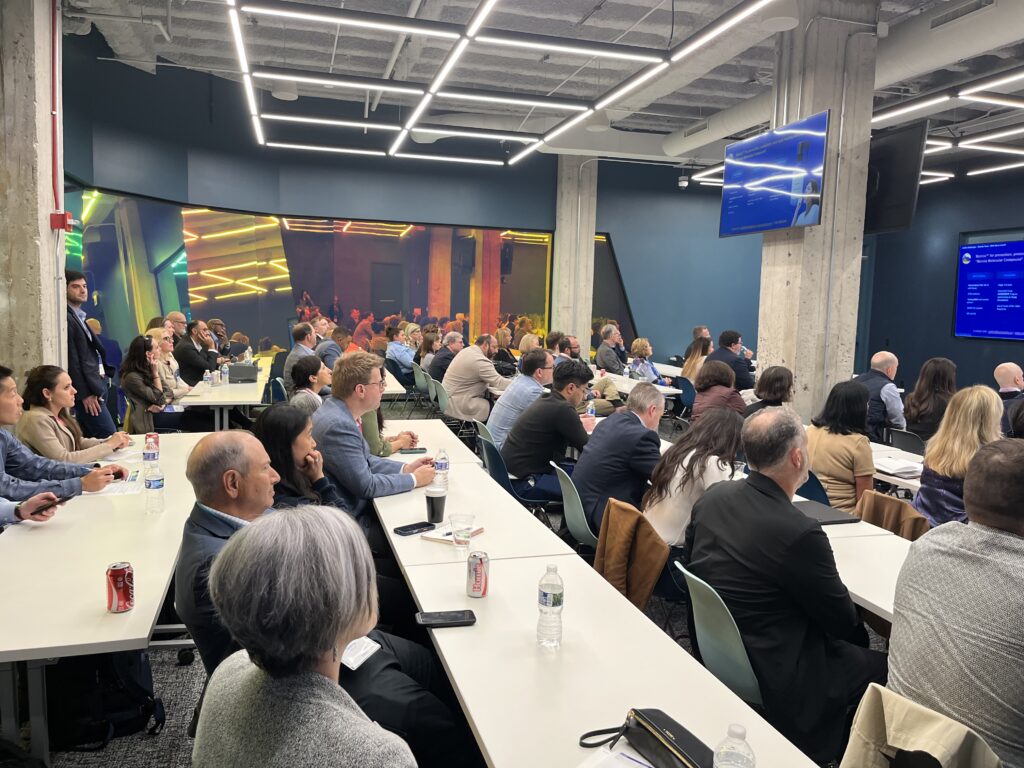 Homepage Investing – CareQuest Innovation Partners Large conference room filled with professionals seated at long tables, watching a presentation on screens at the front.
