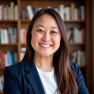 Smiling Asian woman in a navy blazer and white top, posing for a portrait in front of a bookshelf-filled background.