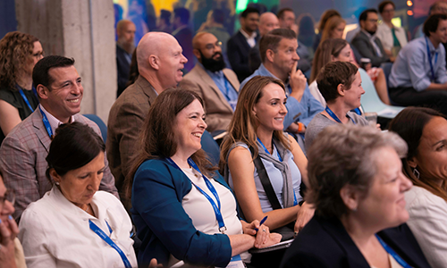 Audience 1 – CareQuest Innovation Partners Diverse conference audience seated in rows, listening attentively with lanyards and smiles.