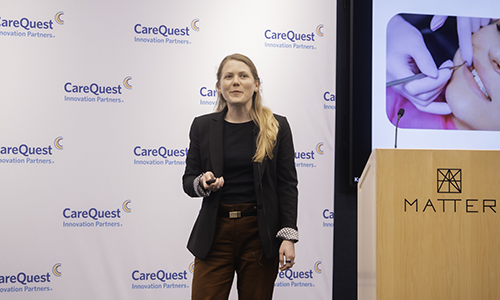 Empallo 1b – CareQuest Innovation Partners Female presenter on a stage with a MATTER podium, speaking, against a CareQuest Innovation Partners backdrop.